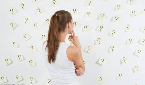 Frau schaut auf eine Wand voller Post-Its mit Fragezeichen